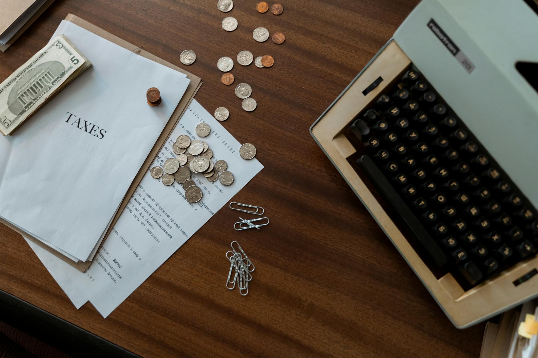 Overhead view of a vintage desk with typewriter, coins, and tax documents.