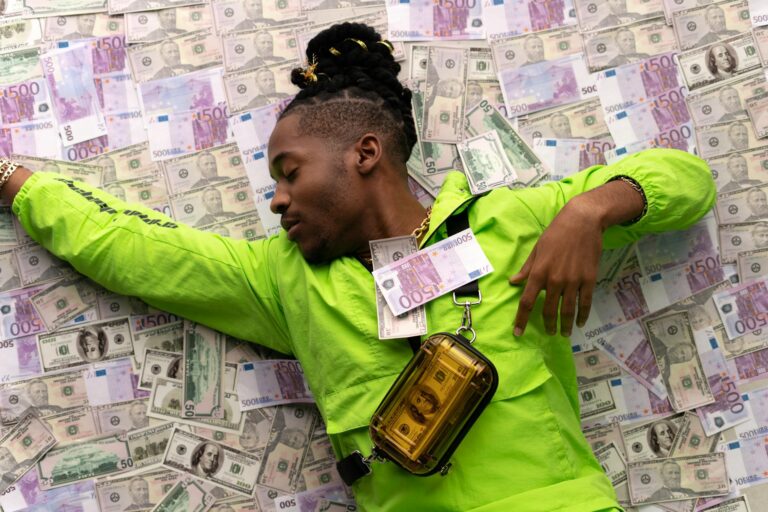 A stylish man in a green jacket lies on a pile of dollar and euro notes, symbolizing wealth.