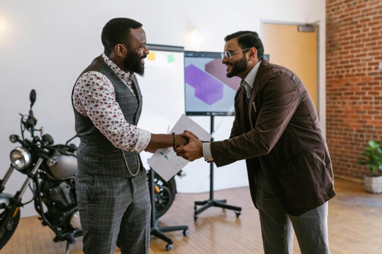 Two male professionals shaking hands in a modern office setting, symbolizing teamwork and collaboration.