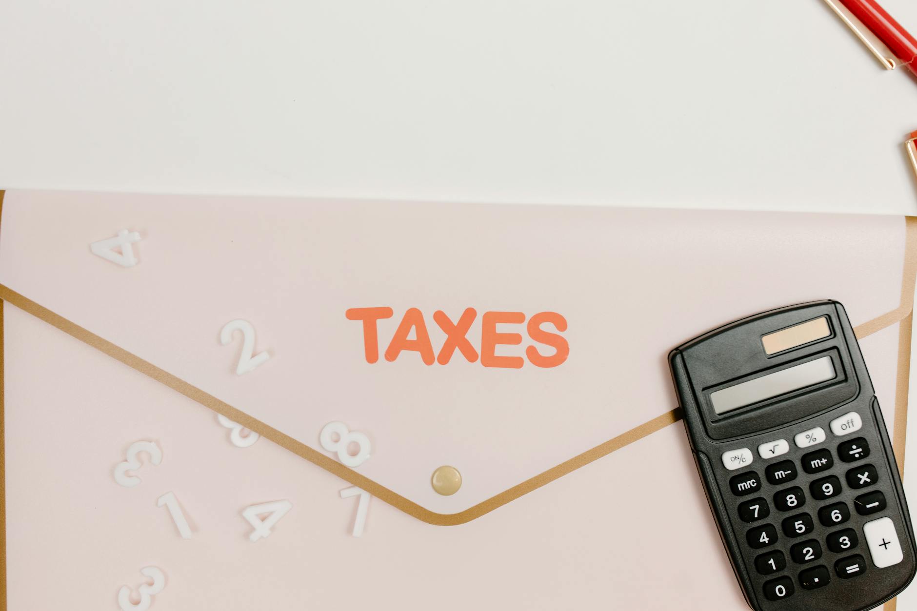 Flat lay of a calculator and folder labeled 'Taxes' for finance and accounting.