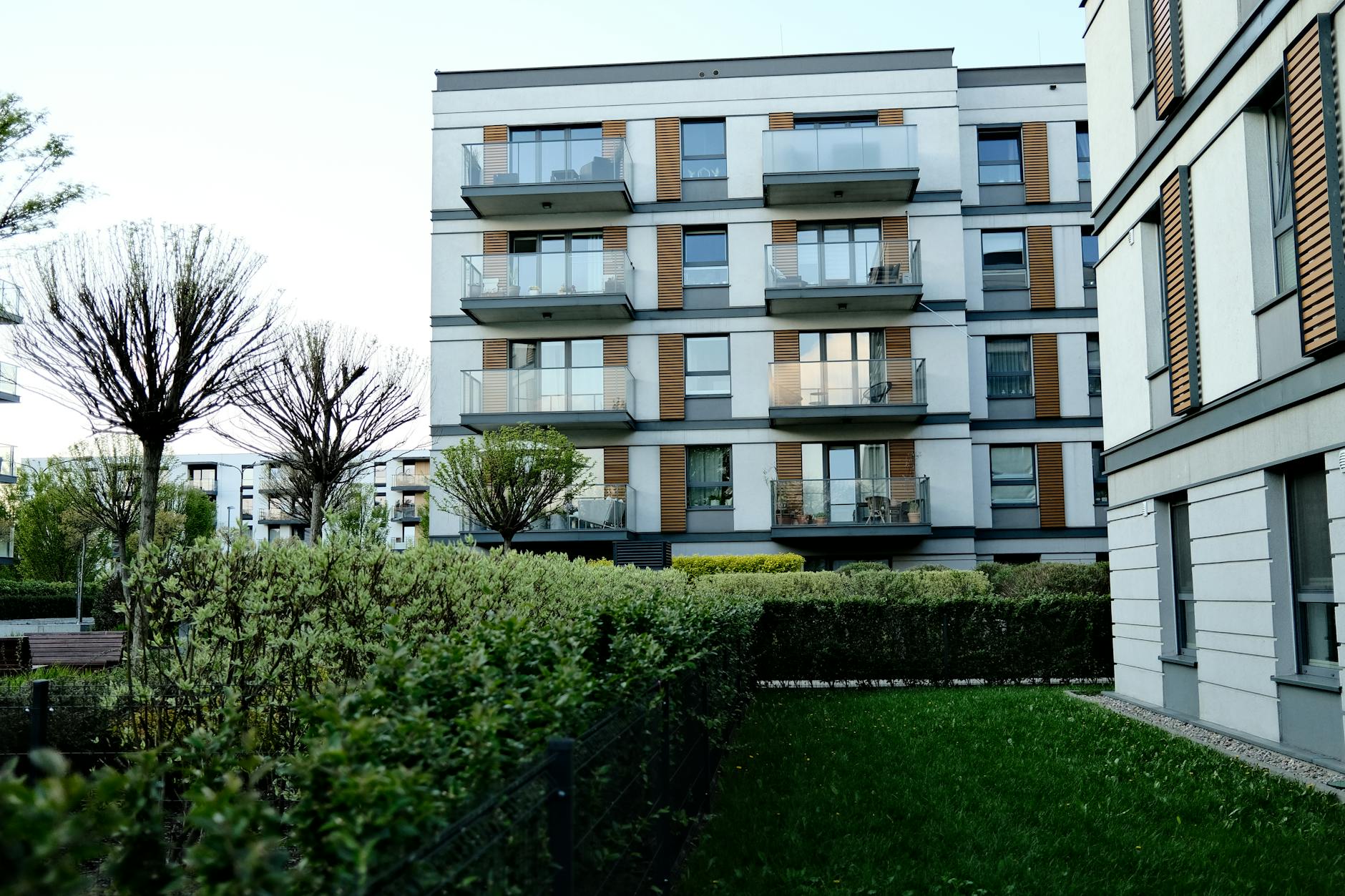 Contemporary apartment complex with balconies and lush garden in urban setting.