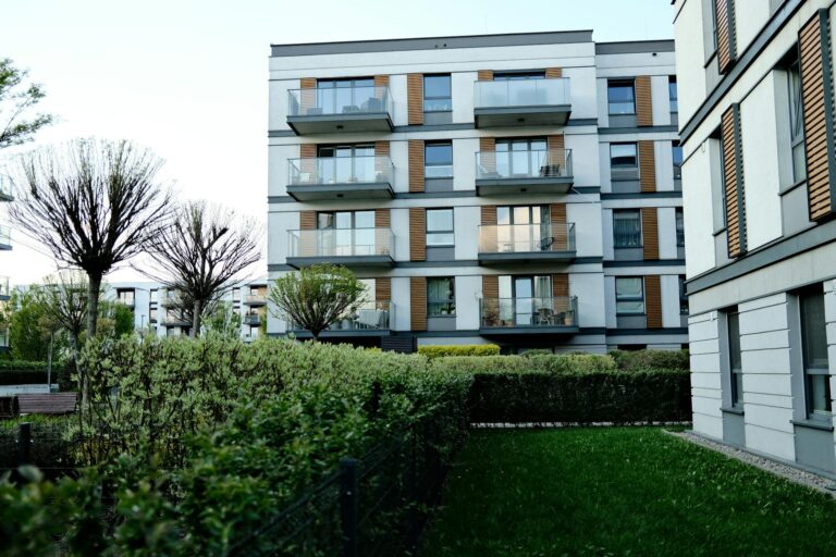 Contemporary apartment complex with balconies and lush garden in urban setting.