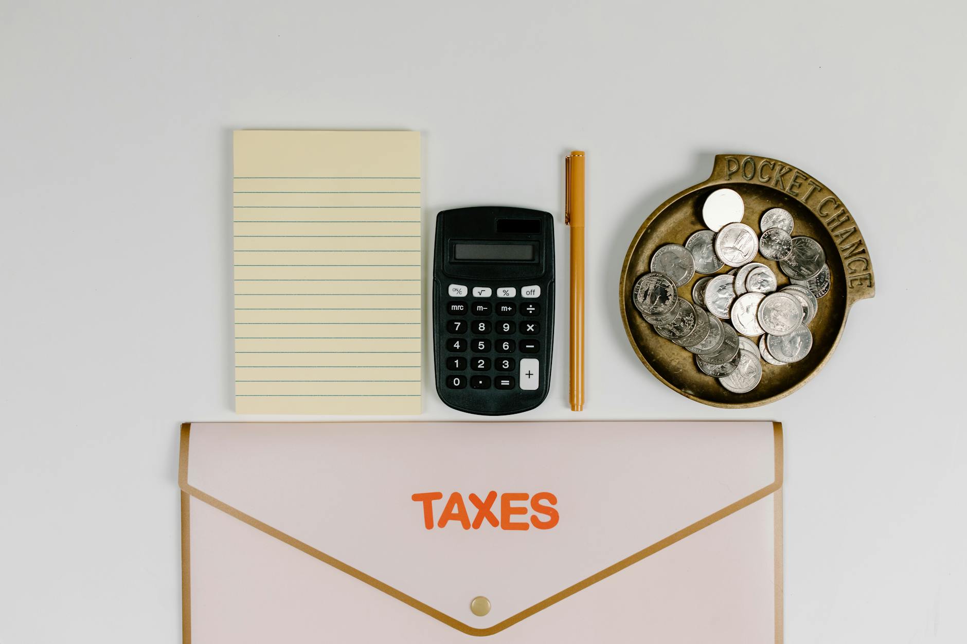 A flat lay of tax preparation essentials: calculator, coins, notepad, pen, and folder.
